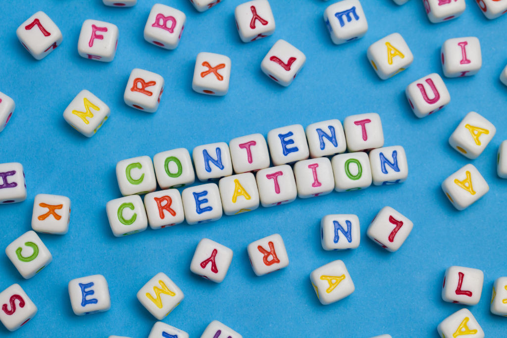 White alphabet beads spelling 'CONTENT CREATION' on a vibrant blue background, surrounded by scattered colourful letter beads, symbolising creativity and the process of generating ideas.